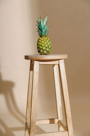 Studio shot of delicious fresh whole pineapple with leaf on chair isolated over beige backgroundの写真素材