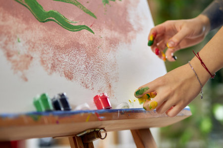 Close up shot of hands in paint of female artist creating abstract painting at home studio workshopの写真素材