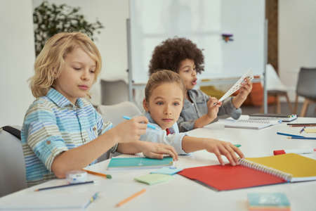 Social activity. Diverse kids sitting together at the table in elementary school classroomの写真素材