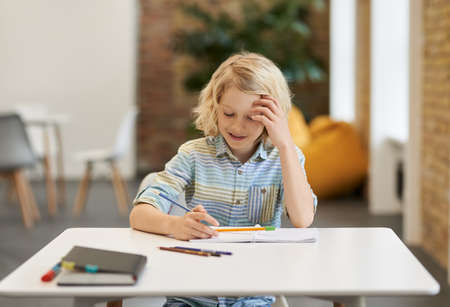 Solve equation. Diligent elementary school boy doing sums, writing in his notebook while sitting at the desk in classroomの写真素材