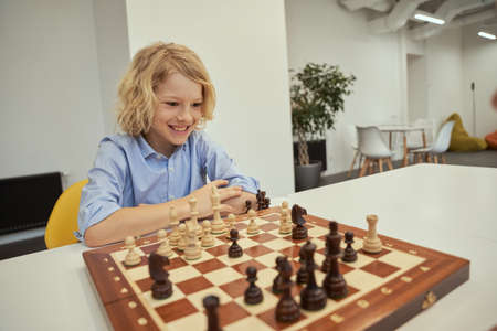 Chess fan. Motivated caucasian boy looking excited while playing chess, sitting at the table in schoolの写真素材