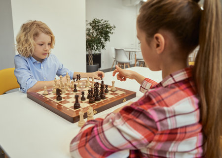Change with each move. Concentrated little caucasian boy planning his move while playing chess with friend, sitting together at the table in schoolの写真素材