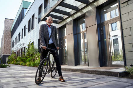 Keep moving. Full length shot of confident mature businessman looking away while standing with his bicycle near modern office building outdoorsの写真素材