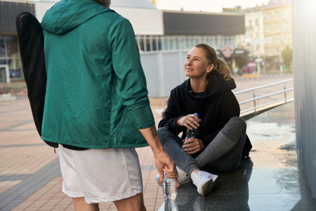 Sportive mature woman woman in sportswear talking with her partner outdoors while waiting together for workoutの写真素材