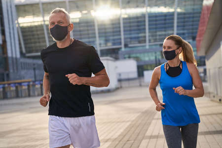 Sportive middle aged couple jogging with protective masks in the morning. Covid19 responsible behaviorの写真素材