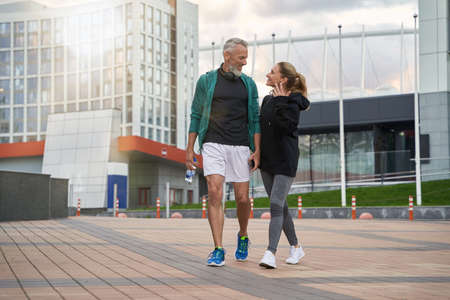 Full length shot of happy sportive middle aged couple in sportswear looking cheerful while walking together outdoors after workoutの写真素材
