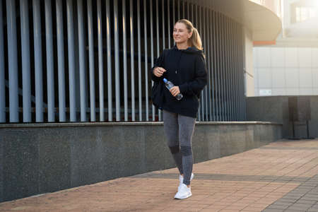 Full length shot of attractive middle aged sportswoman in sportswear smiling while walking outdoors, ready for workoutの写真素材