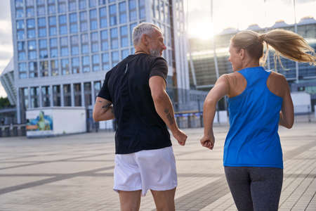 Back view of middle aged couple in sportswear staying active, jogging together in urban environmentの写真素材