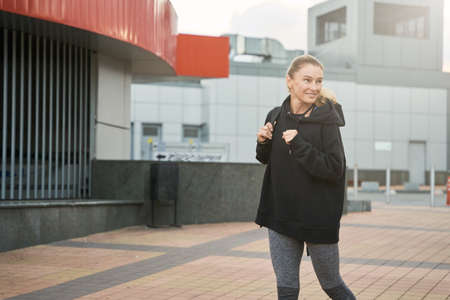 Sportive middle aged woman in sportswear looking away with a smile while walking outdoors after workoutの写真素材