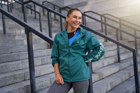 Happy middle aged sportswoman in sportswear smiling away standing outdoors after morning workout in...