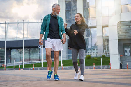 Full length shot of active middle aged couple in sportswear looking cheerful while walking together outdoors after gym workoutの写真素材