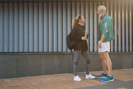 Side view of sportive middle aged people in sportswear looking at each other, talking while standing together outdoors after gym workoutの写真素材