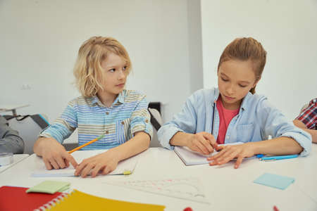 Beautiful little schoolboy and schoolgirl studying and making notes, sitting together at the table in elementary school classroomの写真素材