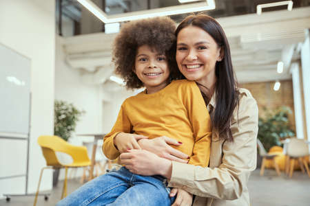 Portrait of cute little boy with afro hair smiling while posing for camera together with beautiful young female teacherの写真素材