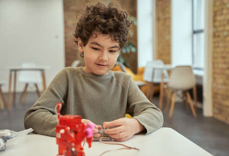 Learn how it works. Lovely little boy sitting at the table, checking technical toy full of details,...