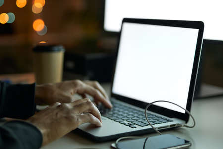 Close up shot of hands of man sitting at the table in front of computer monitor and using laptop while working late at nightの写真素材