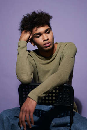 Portrait of young latino man sitting on black chair in studio. Handsome transgender male in casualの写真素材
