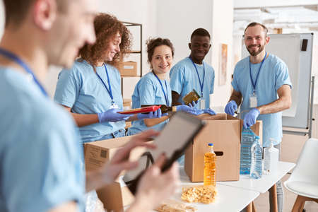 Smiling diverse volunteers sorting foodstuff in cardboard boxes, working together on donation projectの写真素材