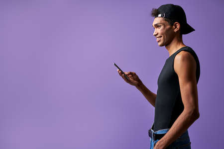 Smiling male with mobile in hand side view on purple background portraitの写真素材