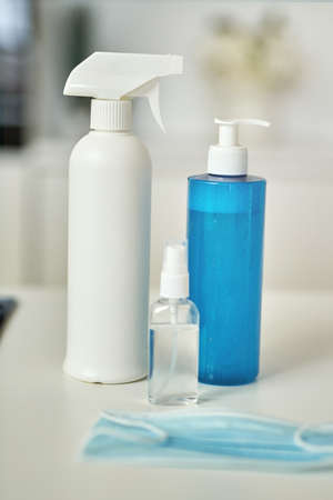 Close up shot of detergents, sanitizer spray and gel in bottles, protective face mask on kitchen surfaceの写真素材