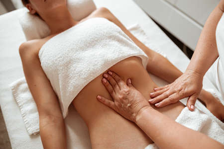 Masseuse massaging female client abdomen at wellness centerの写真素材