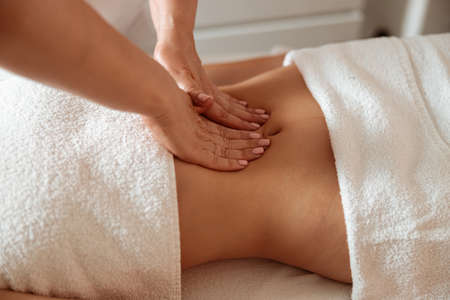 Masseuse massaging female client abdomen in spa salonの写真素材