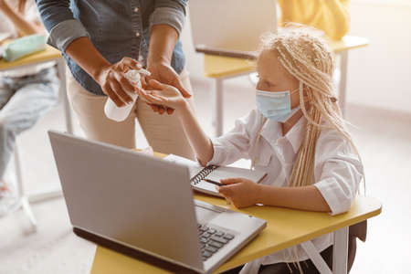 Schoolgirl in a protective mask disinfecting her hands at school