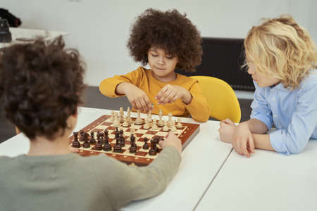 Awesome little children discussing game while sitting at the table and playing chess indoorsの写真素材