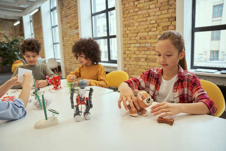 Science is everywhere. Positive diverse children spending time at engineering club. Girl sitting at the table, playing with technical toyの写真素材