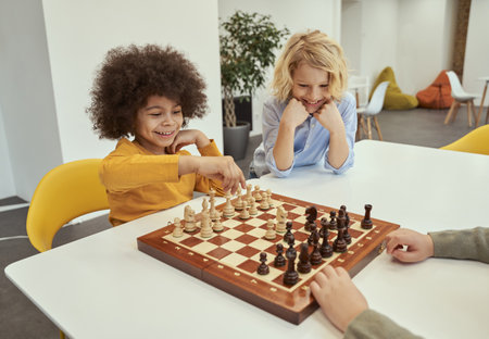 Smiling little diverse boys sitting together at the table and playing chess in schoolの写真素材