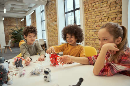 Making learning fun. Ambitious diverse kids having fun together while examining details of technical toys, sitting at the table during STEM classの写真素材