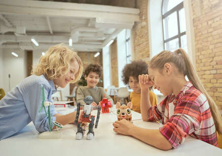 Development. Joyful diverse children sitting at the table, looking at technical toys full of details, spending time at engineering clubの写真素材