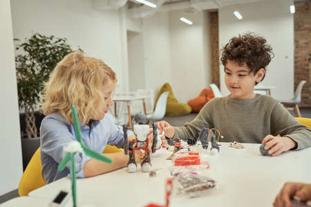 Learn from your own experience. Cheerful little boys examining and playing with robots, sitting at the table during STEM classの写真素材