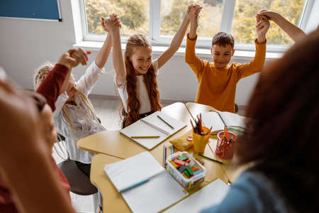 Schoolchildren sitting at the table and raising their hands upの写真素材