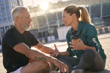 Portrait of sportive mature couple communicating with each other while sitting outdoors on a sunny summer dayの写真素材