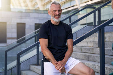 Cheerful middle aged man in perfect shape smiling at camera while posing, standing outdoors in the cityの写真素材