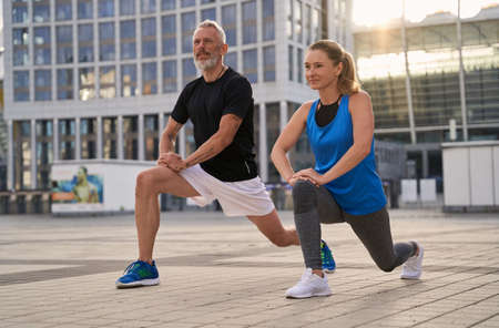 Sporty mature couple, man and woman warming up, getting ready for running together in the city on a summer dayの写真素材