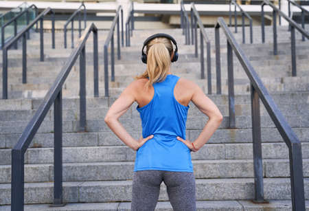 Back view of sportswoman in headphones standing outdoors while having workout in the cityの写真素材