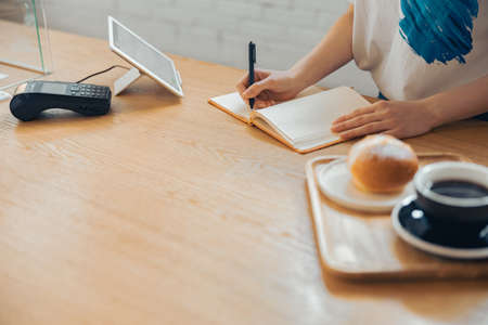 Female barista writing in notebook in coffee shopの写真素材