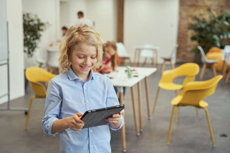 Portrait of clever little boy smiling, using tablet pc while posing for camera during STEM classesの写真素材