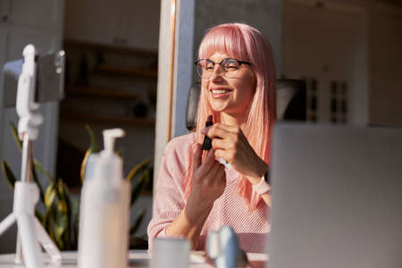 Beautiful lady blogger shows purple lipstick recording video at table with cosmetic productsの写真素材