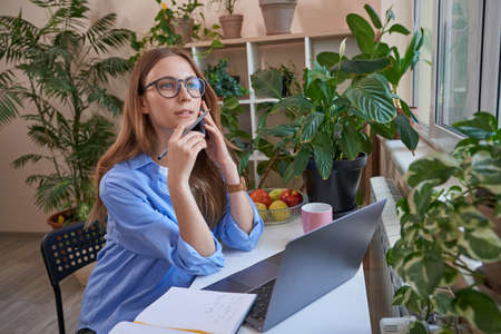 Woman in glasses using phone while talking during learning at home onlineの写真素材