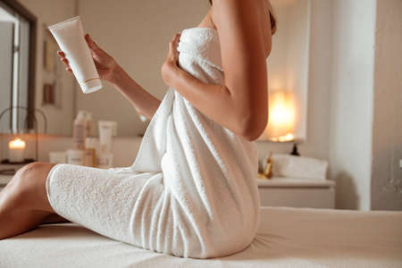 Young woman with cosmetic product in hand relaxing in spa salonの写真素材