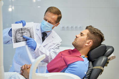 Worried dental surgeon holding an x-ray image near his patientの写真素材