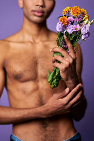Close-up portrait of nude torso of boy with flowers in hand. Sensual latino young man posingの写真素材
