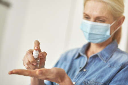 Close up shot of woman in protective face mask cleaning her hands using antibacterial hand sanitizer gel pump dispenserの写真素材