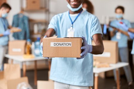 Close up shot of cardboard box for Donation in hands of african american young male volunteer in...