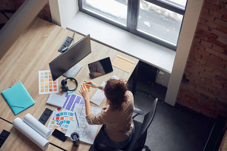 High angle view of female designer using sticky notes, working on new interior design project,...