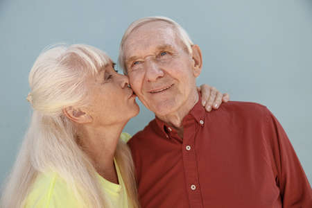 Blonde mature woman kisses loving partner standing on light grey backgroundの写真素材