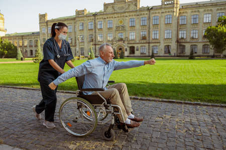 Full length shot of cheerul aged man, recovering patient making gesture on a walk with caring nurse in the park near hospitalの写真素材
